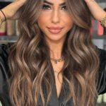 Woman with long, dimensional brunette balayage and voluminous waves, showcasing professional hair color at Silver Palm Salon in Littleton, CO
